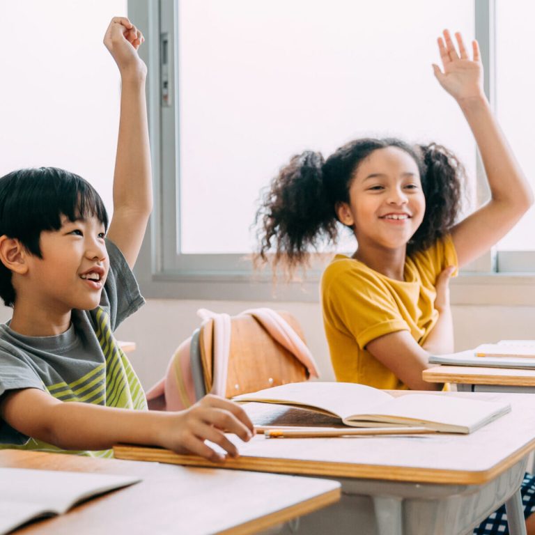 Elementary age Asian student boy raised hands up in class. Diverse group of pre-school pupils in elementary age in education building school. Volunteering and participating classroom concept.